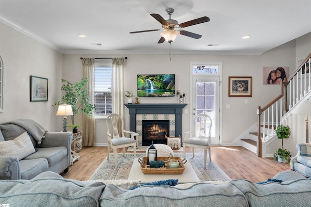 living area with visible vents, a ceiling fan, wood finished floors, crown molding, and stairs