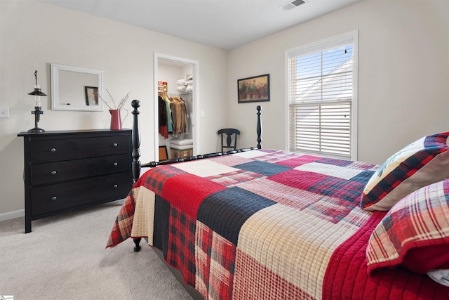 bedroom featuring visible vents, a walk in closet, baseboards, light carpet, and a closet