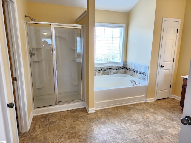 bathroom with stone finish floor, vanity, baseboards, a garden tub, and a stall shower