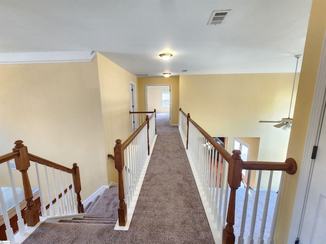 corridor with carpet floors, visible vents, baseboards, and an upstairs landing