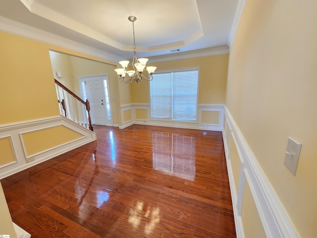 unfurnished dining area with a tray ceiling, an inviting chandelier, wood finished floors, stairway, and a decorative wall