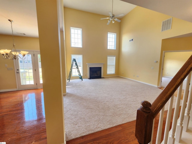 unfurnished living room with visible vents, baseboards, a high ceiling, a fireplace with flush hearth, and ceiling fan with notable chandelier