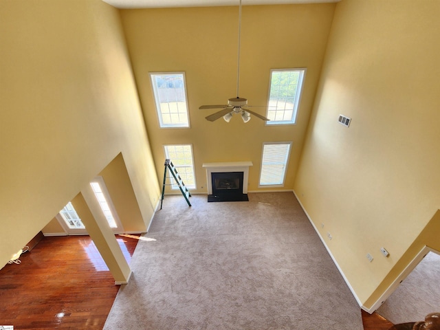 unfurnished living room with carpet flooring, a high ceiling, plenty of natural light, and ceiling fan