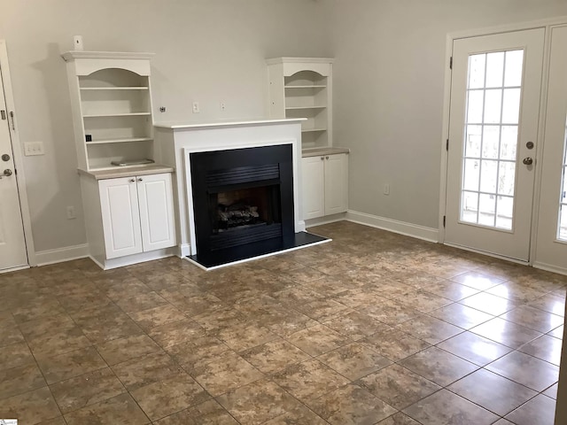 unfurnished living room featuring baseboards and a fireplace with raised hearth