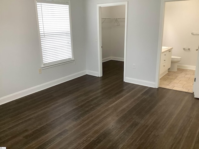 unfurnished bedroom featuring a spacious closet, baseboards, a closet, and dark wood-style flooring