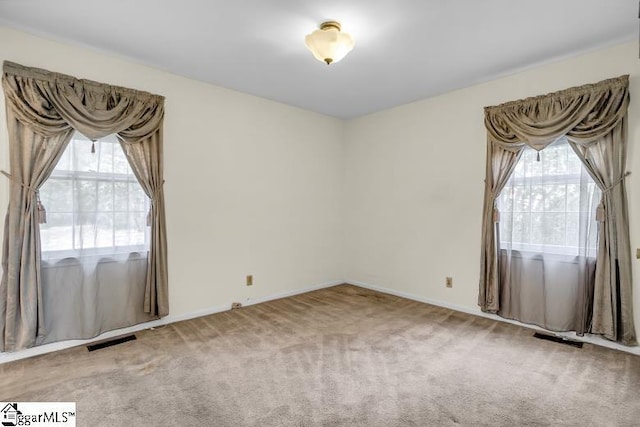 carpeted empty room featuring visible vents, a healthy amount of sunlight, and baseboards