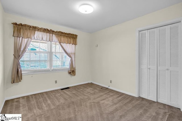 unfurnished bedroom with carpet flooring, baseboards, visible vents, and a closet