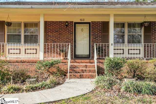 doorway to property featuring brick siding and covered porch