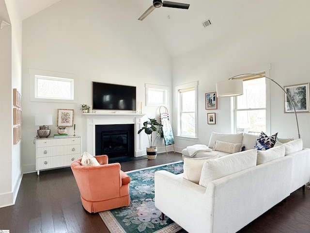 living room featuring visible vents, ceiling fan, dark wood finished floors, a fireplace with flush hearth, and high vaulted ceiling