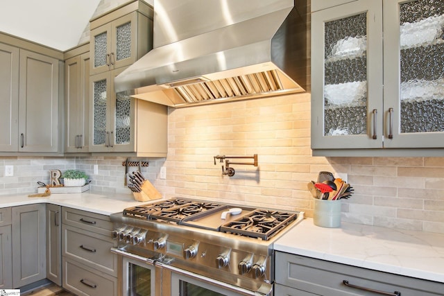 kitchen featuring gray cabinets, double oven range, tasteful backsplash, wall chimney range hood, and glass insert cabinets