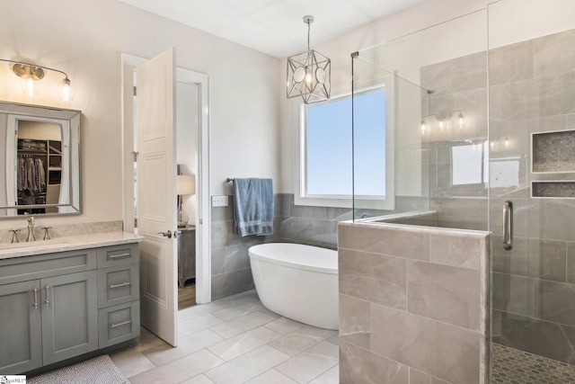 bathroom with a chandelier, vanity, a stall shower, a freestanding tub, and tile walls