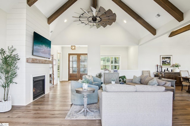 living room featuring visible vents, beamed ceiling, a fireplace, wood finished floors, and high vaulted ceiling