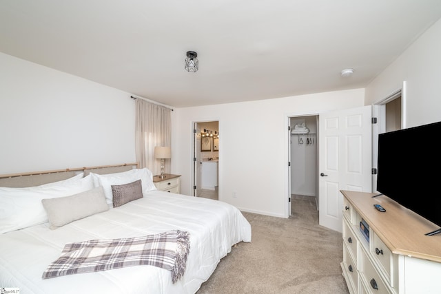 bedroom featuring a spacious closet, connected bathroom, baseboards, and light carpet