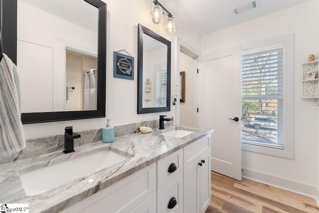 full bath with a sink, visible vents, wood finished floors, and double vanity