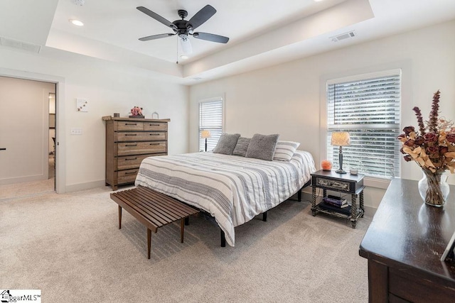 bedroom with visible vents, light colored carpet, and a tray ceiling