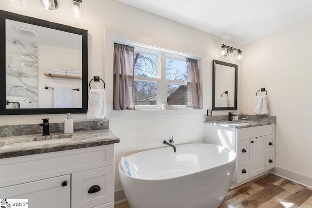 bathroom featuring a freestanding tub, wood finished floors, two vanities, and a sink