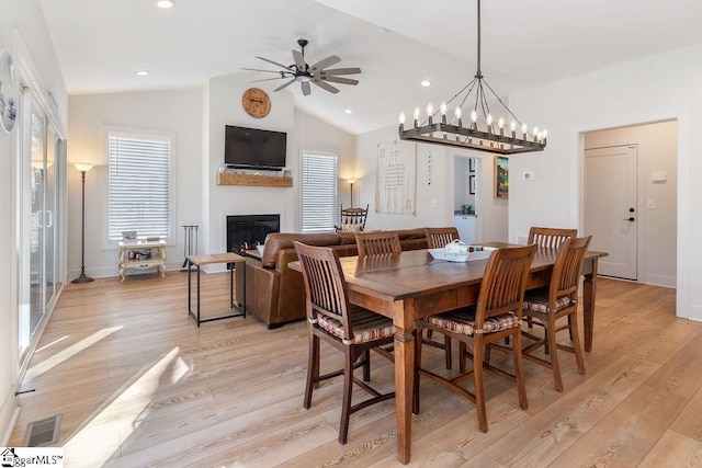 dining room with visible vents, a glass covered fireplace, light wood finished floors, ceiling fan, and vaulted ceiling