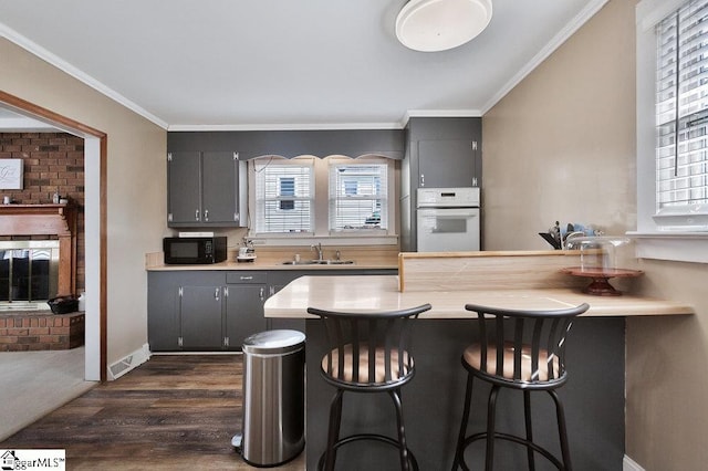 kitchen with black microwave, a breakfast bar area, ornamental molding, white oven, and a sink