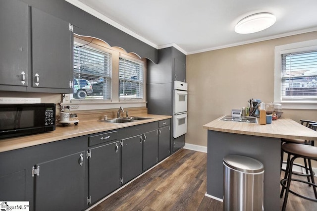 kitchen featuring a sink, crown molding, black microwave, a breakfast bar, and dark wood-style flooring