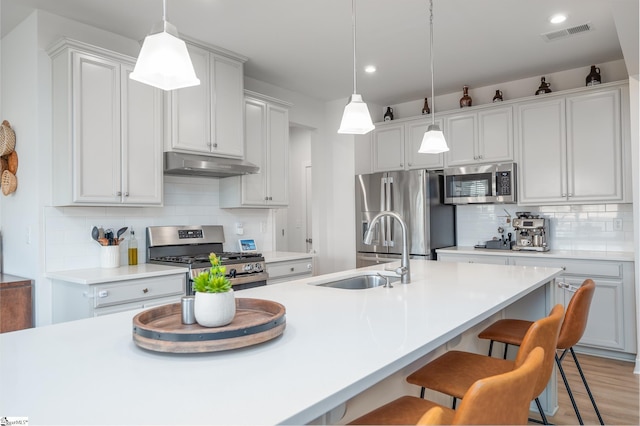 kitchen with visible vents, under cabinet range hood, a sink, a kitchen breakfast bar, and appliances with stainless steel finishes