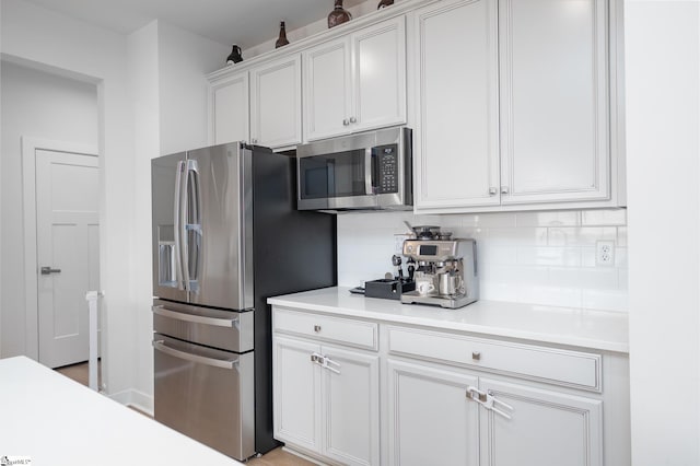 kitchen with backsplash, appliances with stainless steel finishes, white cabinetry, and light countertops