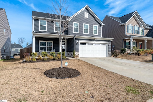 traditional-style house with stone siding, covered porch, concrete driveway, an attached garage, and central AC unit