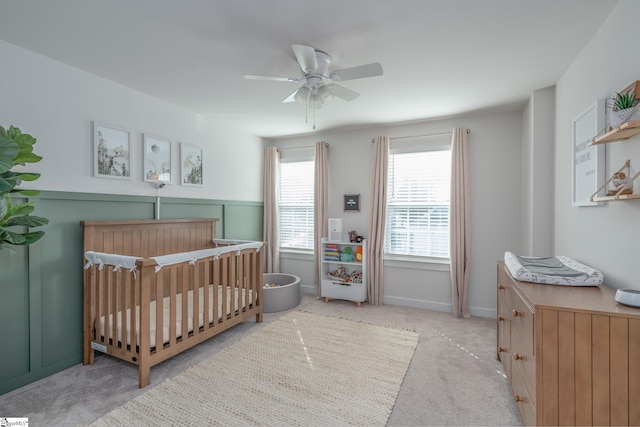 bedroom featuring ceiling fan, a nursery area, baseboards, and light carpet