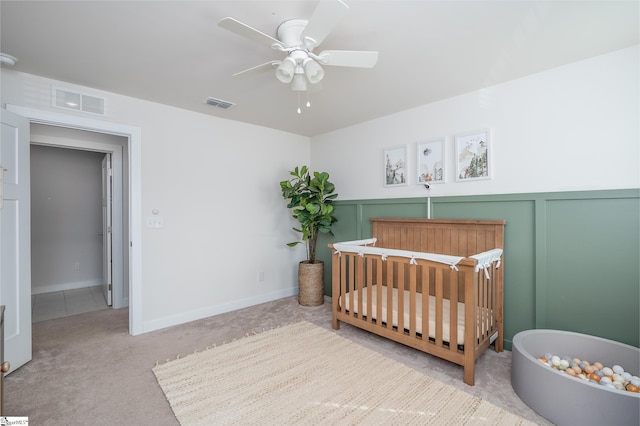 carpeted bedroom with a crib, a decorative wall, a ceiling fan, and visible vents