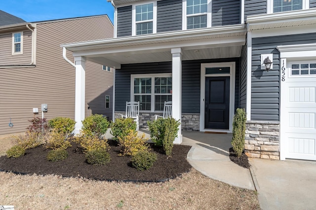 doorway to property featuring a garage, stone siding, and covered porch