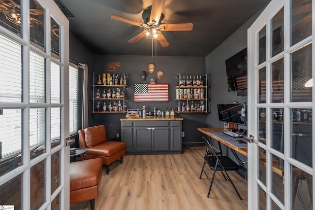 office with light wood finished floors, a dry bar, french doors, and a ceiling fan