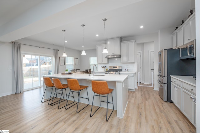 kitchen with a sink, stainless steel appliances, light countertops, a kitchen breakfast bar, and backsplash