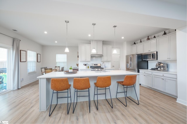 kitchen featuring light wood-type flooring, tasteful backsplash, appliances with stainless steel finishes, and a breakfast bar