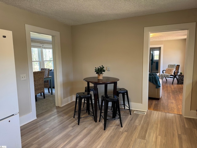 dining space featuring visible vents, baseboards, a textured ceiling, and wood finished floors