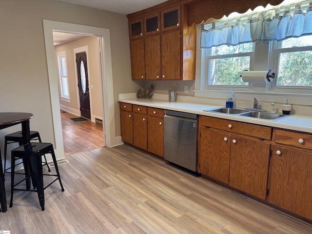 kitchen with stainless steel dishwasher, light countertops, light wood-type flooring, and a sink