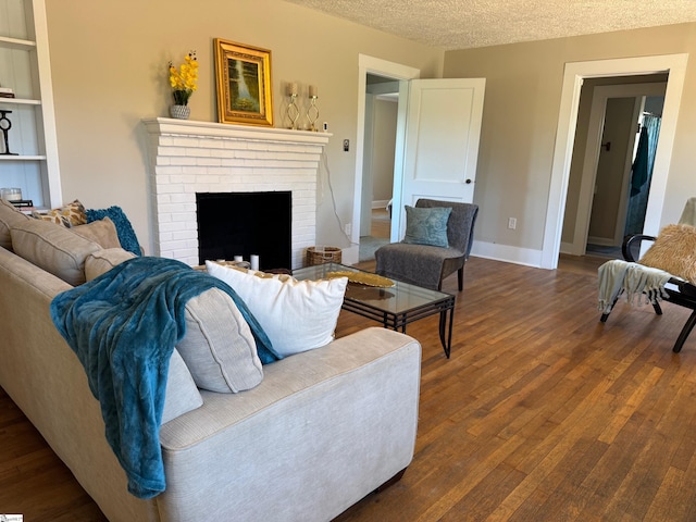 living room featuring built in shelves, a textured ceiling, dark wood-style floors, baseboards, and a brick fireplace