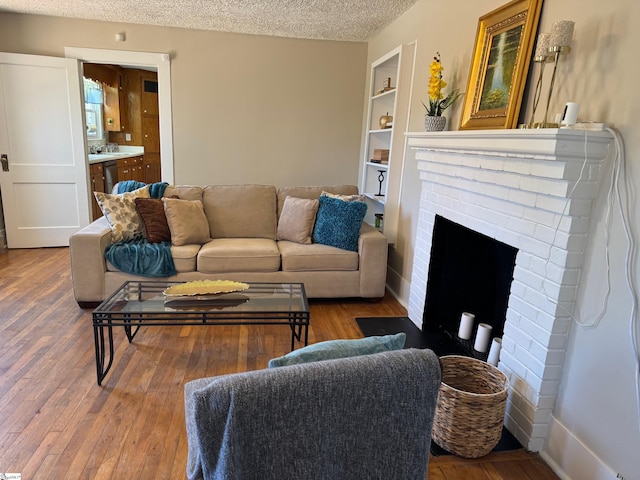 living room featuring built in shelves, a textured ceiling, a brick fireplace, and hardwood / wood-style floors