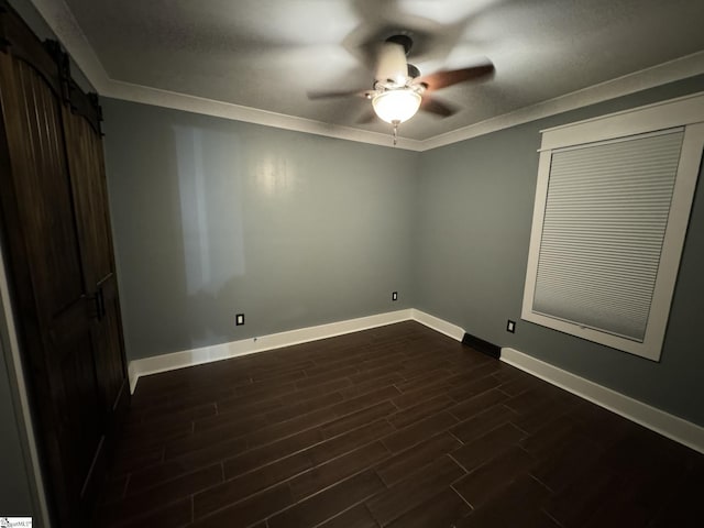 empty room featuring a barn door, dark wood-type flooring, ceiling fan, and crown molding