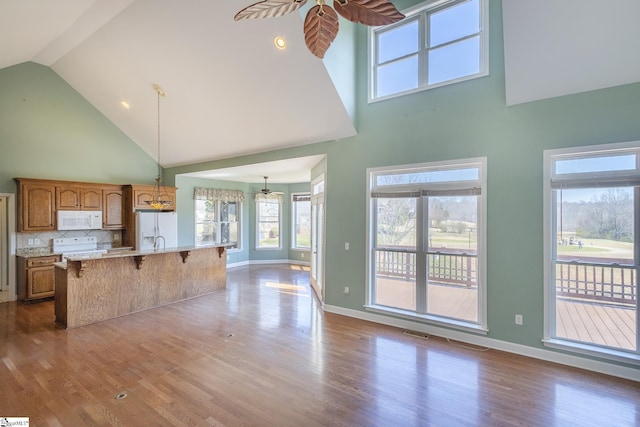 kitchen with an island with sink, a kitchen bar, dark wood-style floors, white appliances, and a ceiling fan