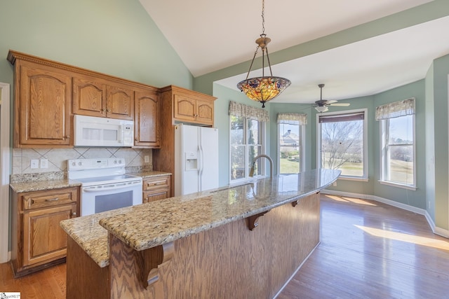 kitchen featuring a breakfast bar, tasteful backsplash, wood finished floors, white appliances, and light stone countertops