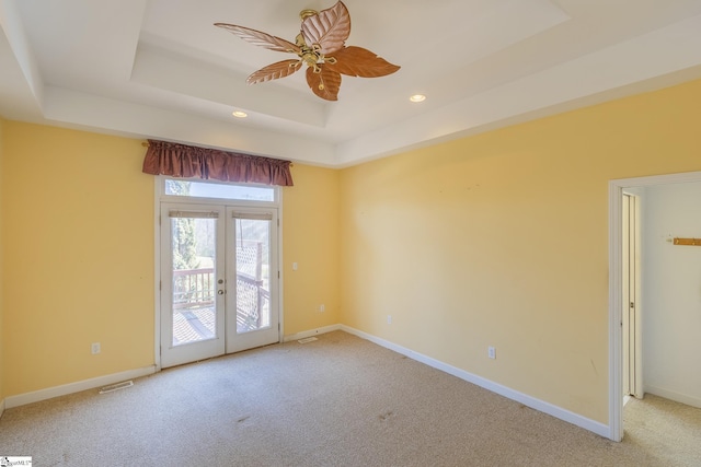 carpeted spare room featuring visible vents, baseboards, a tray ceiling, french doors, and a ceiling fan