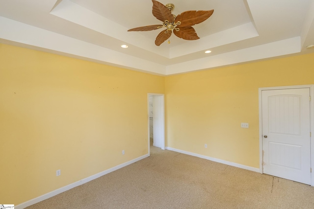 spare room with light carpet, ceiling fan, a raised ceiling, and baseboards