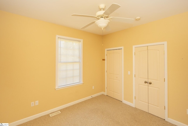 unfurnished bedroom featuring visible vents, light carpet, multiple closets, a ceiling fan, and baseboards