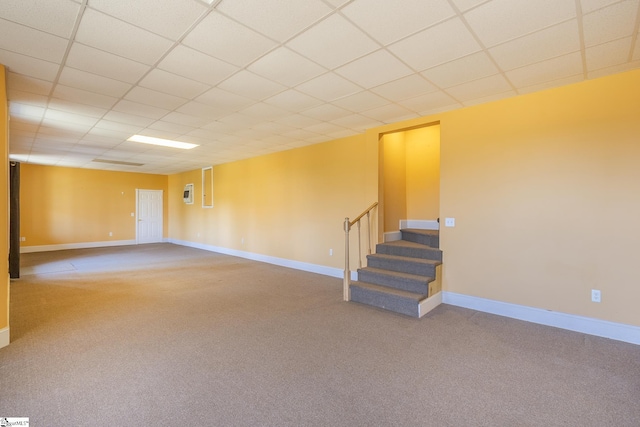 basement with a paneled ceiling, stairs, and carpet