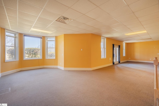 carpeted spare room featuring baseboards, visible vents, and a drop ceiling