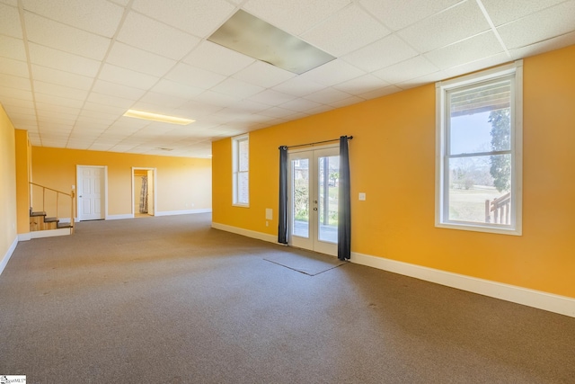 carpeted empty room with a drop ceiling and baseboards