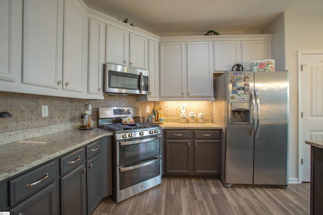 kitchen with light stone countertops, decorative backsplash, stainless steel appliances, wood finished floors, and white cabinetry