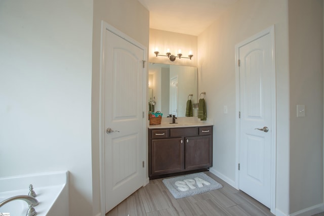 bathroom featuring vanity, wood finished floors, a bathing tub, and baseboards