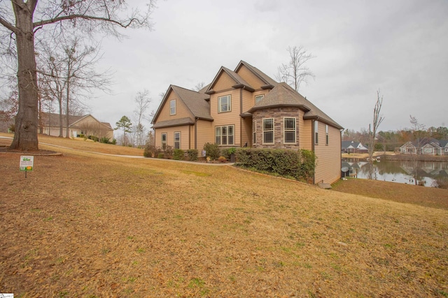 view of front of property with stone siding, a front yard, and a water view