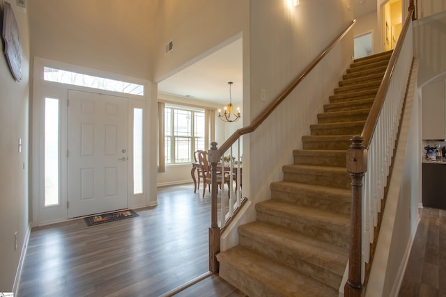 foyer entrance with stairway, visible vents, dark wood finished floors, a high ceiling, and a notable chandelier