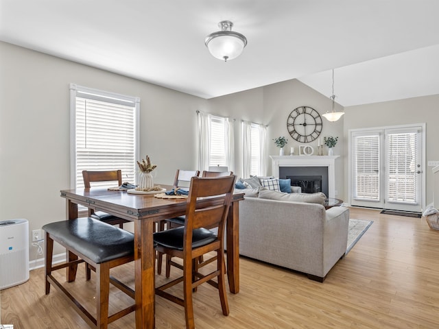 dining room with light wood-style floors, a healthy amount of sunlight, a glass covered fireplace, and vaulted ceiling